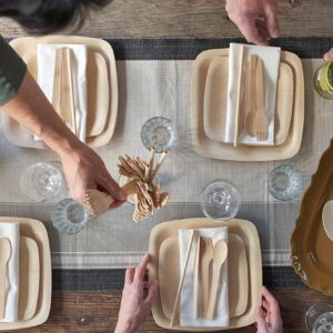 A dining table shown above, set with bamboo plates, straws and utensils.