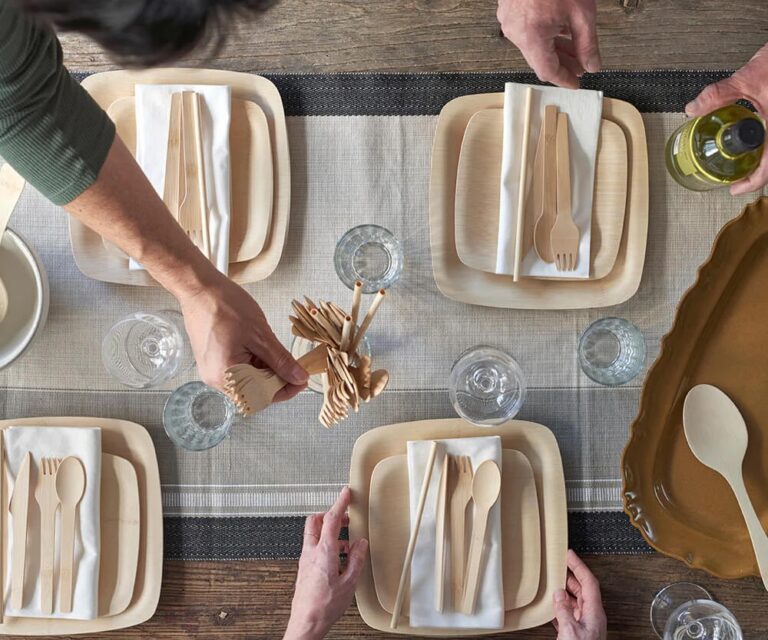 A dining table shown above, set with bamboo plates, straws and utensils.