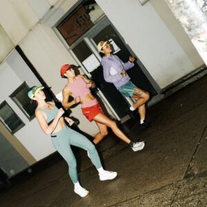 Three women running on an urban sidewalk in colorful clothes.