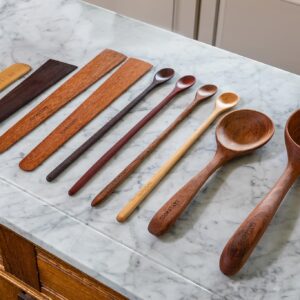 Wooden cooking utensils in different colors of wood laid out on a white marble countertop.