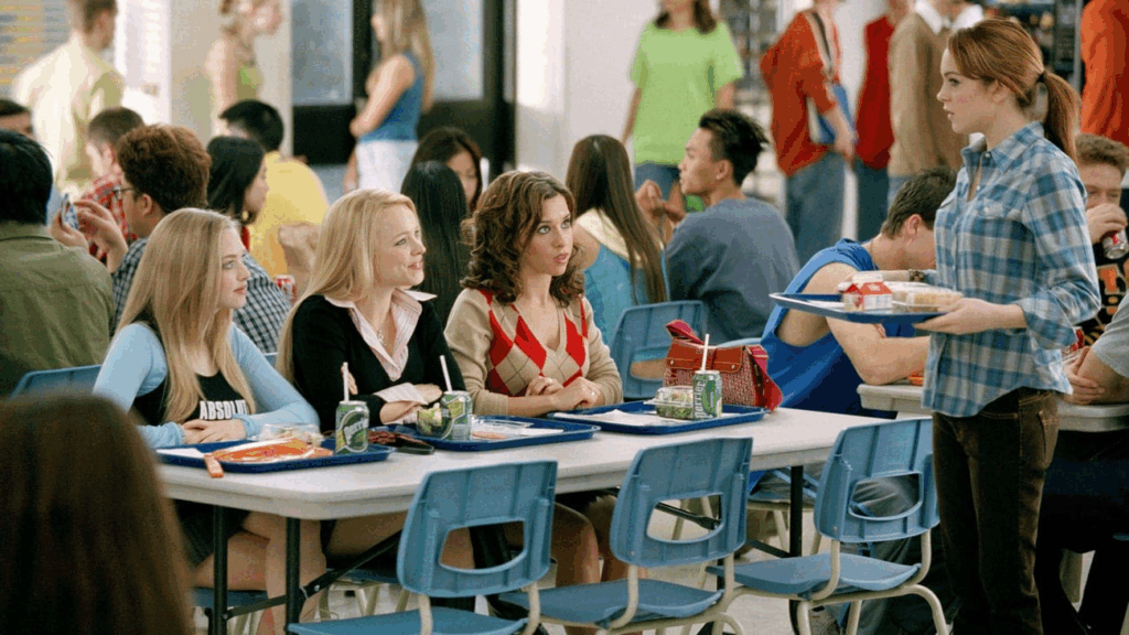 Several pretty high-school aged girls sit at a table in a busy school cafeteria in a scene from the movie "Mean Girls."