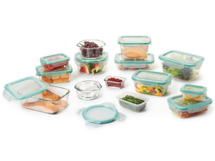 An assortment of OXO Smart Seal glass food storage containers with turquoise lids with various foods in them, including lettuces, grapes, sliced melon, cooked salmon, and chopped bell peppers.