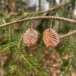 Copper earrings hang on a tree.