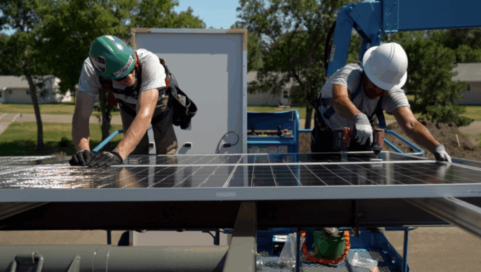 two workers install solar panels on a roof