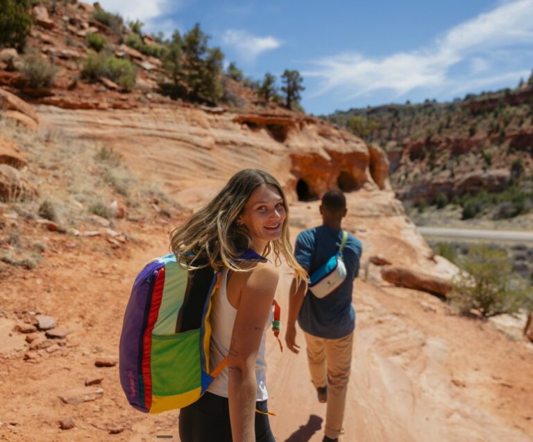 Two people hiking carrying colorful bags from Cotopaxi in the bag's signature assorted bright colors.