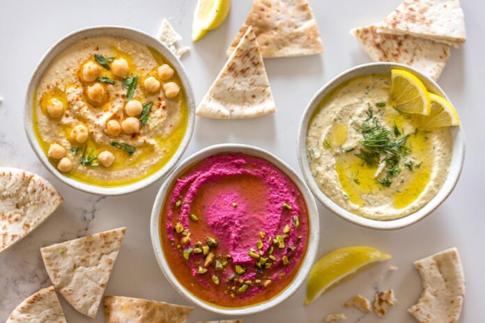 three bowls of hummus served with pita bread