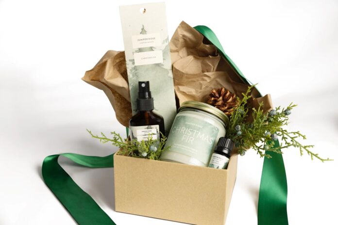 a candle, incense, essential oil, and room spray labeled as Christmas Fir scent products from the brand Juniper Ridge, all in a cardboard box with a big green ribbon