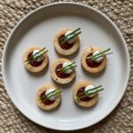 six vegan parmesan linzer cookies topped with pepper jelly and ricotta served on a plate