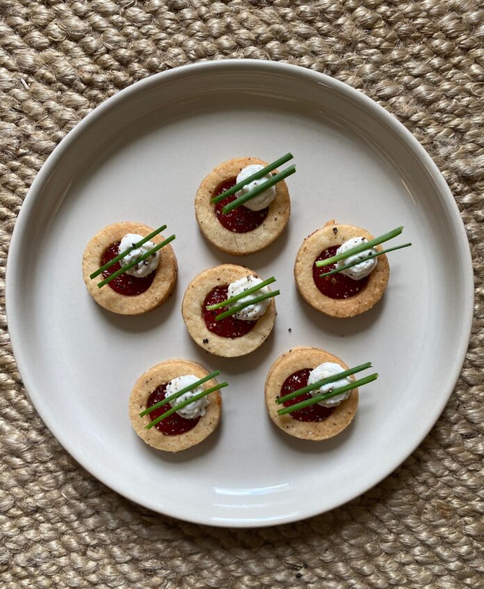 six vegan parmesan linzer cookies topped with pepper jelly and ricotta served on a plate