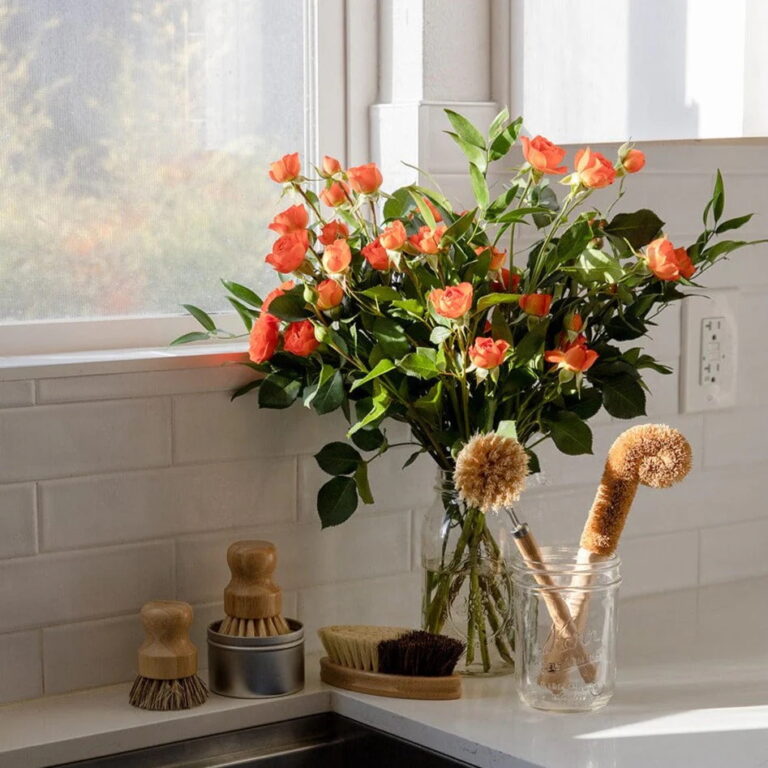 A sink with a bouquet of flowers and natural wood and plant bristle dish brushes.