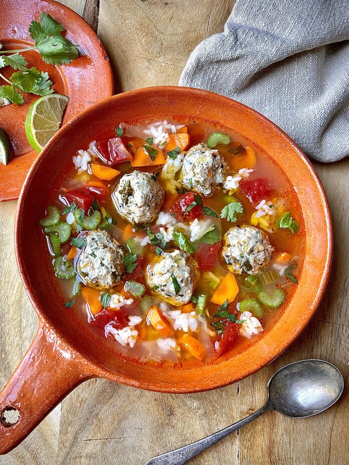 a vibrant chicken albondigas soup served in an orange pan