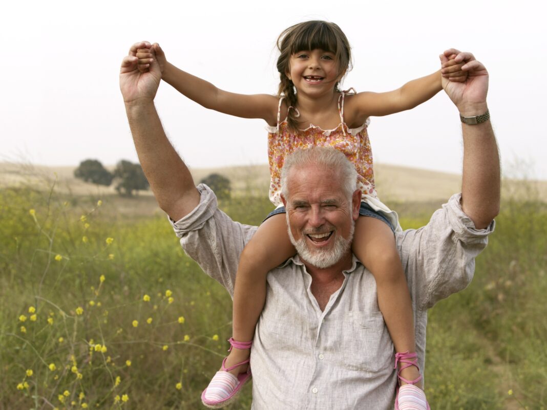 a man holding a child on his shoulders in a field