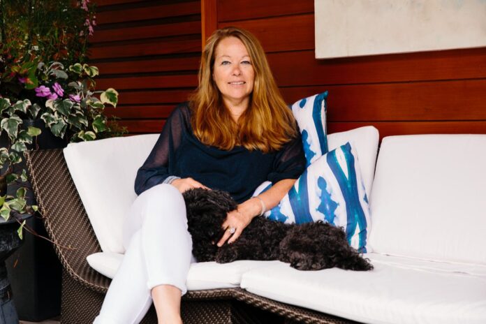 linda cabot sits on a white couch with her dog laying near her lap