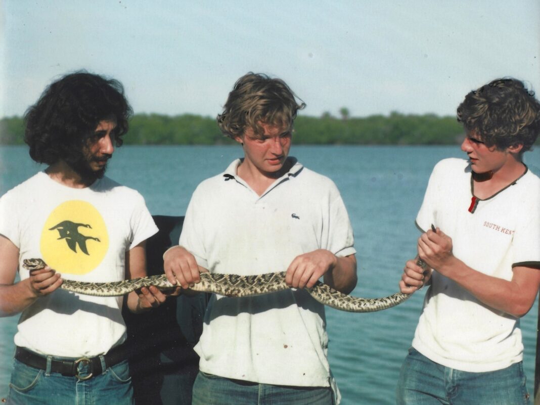tom chase (left) with two other young men, holding a snake