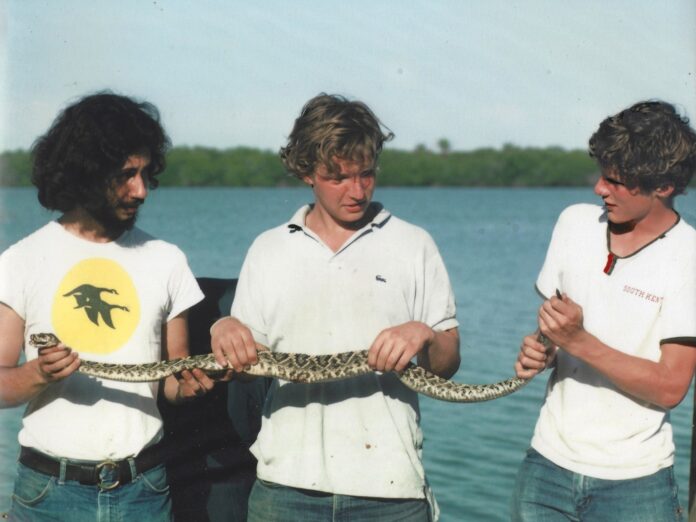 tom chase (left) with two other young men, holding a snake