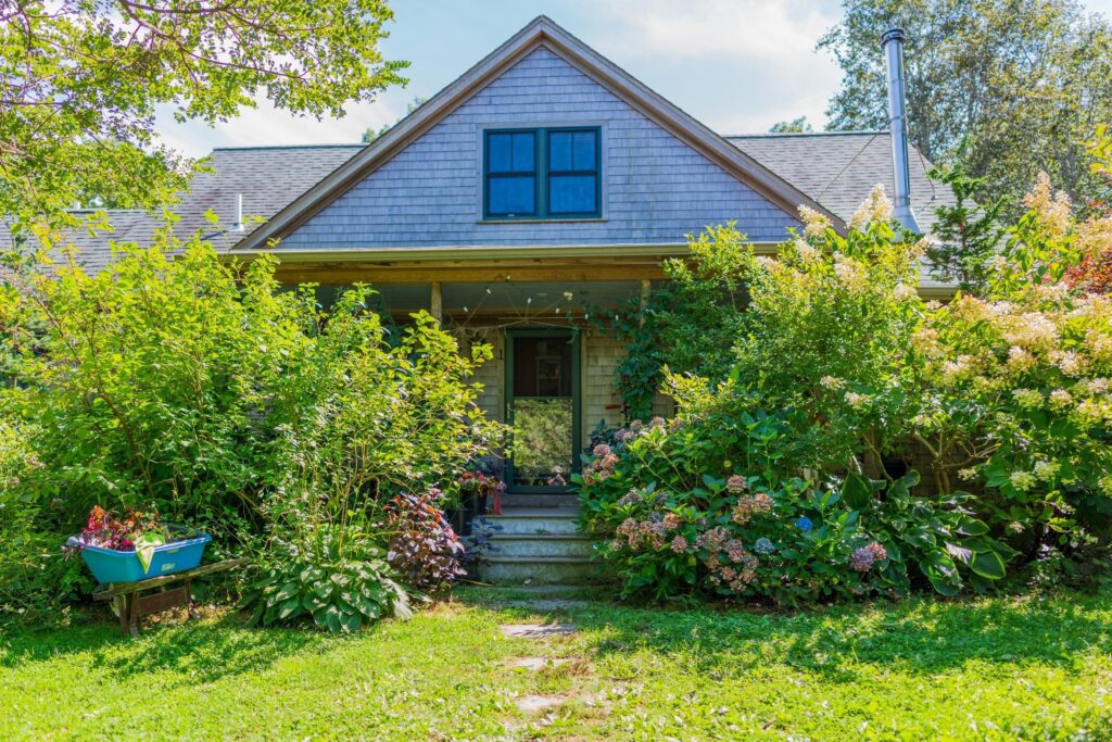 the front of a house with dogwood shrubs on the porch and hydrangeas on the right