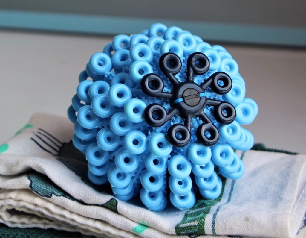 blue cora ball microplastic filter, A squiggly-looking light blue and navy ball on top of folded pieces of fabric.