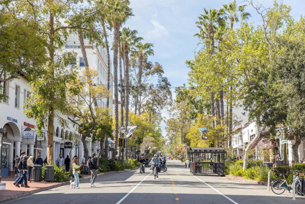 people biking down a street covered in trees in santa barbara