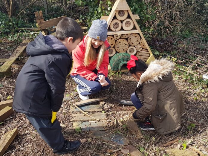 three children outside playing with a wood structure